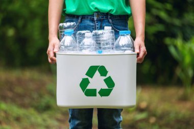 Elinde plastik şişelerle geri dönüşüm kutusunu tutan bir kadın.