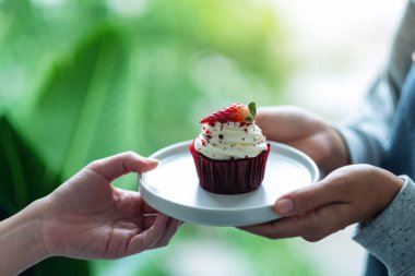 Bir garson müşteriye kırmızı kadife kek ikram ediyor.