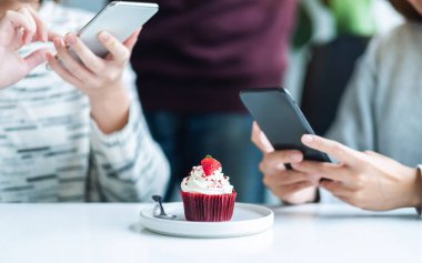 İnsanlar kafede yemeden önce kek fotoğrafı çekmek için cep telefonu kullanıyor.