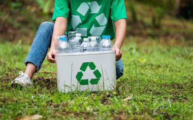 Açık havada plastik şişe toplayıp geri dönüşüm kutusuna koyan bir kadın.