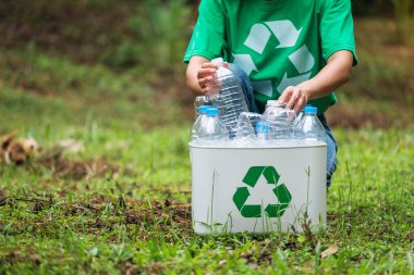 Açık havada plastik şişe toplayıp geri dönüşüm kutusuna koyan bir kadın.