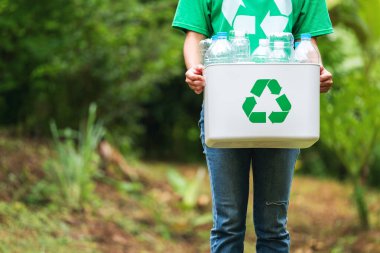 Elinde plastik şişelerle geri dönüşüm kutusunu tutan bir kadın.