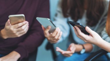 Bir grup genç yan yana otururken cep telefonu kullanıyor ve bakıyor