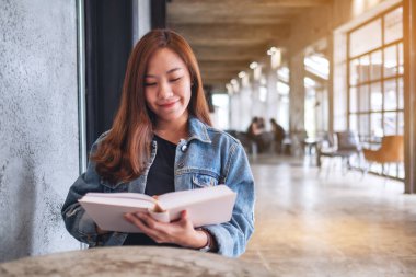 Oturup kitap okuyan Asyalı güzel bir kadının portresi.