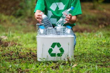 Açık havada plastik şişe toplayıp geri dönüşüm kutusuna koyan bir kadın.