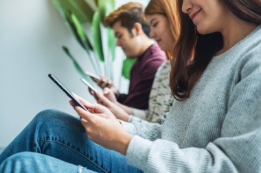 Bir grup genç yan yana otururken cep telefonu kullanıyor ve bakıyor