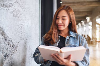 Oturup kitap okuyan Asyalı güzel bir kadının portresi.