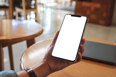 Masasında dizüstü bilgisayarı olan, boş beyaz masaüstü ekranlı cep telefonu tutan bir kadının görüntüsü.