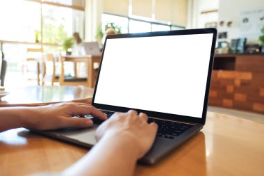 Laptop bilgisayar klavyesinde yazı yazan ve kullanan bir kadının resmi. Tahta masadaki boş beyaz masaüstü ekran.