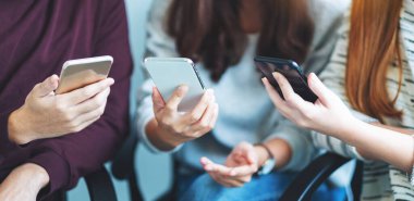 Bir grup genç yan yana otururken cep telefonu kullanıyor ve bakıyor