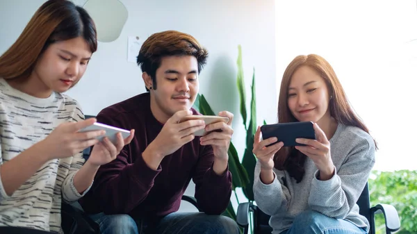 Bir grup genç birlikte otururken cep telefonuyla oyun oynuyor ve kullanıyor