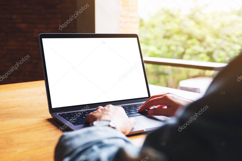 Mockup image of a woman using and typing on laptop computer keyboard with blank white desktop screen on wooden table