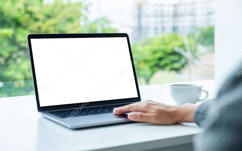 Mockup image of a hand using and touching on laptop touchpad with blank white desktop screen in office