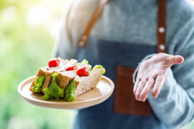 Yakından bakınca, servis yapan bir garsonun ahşap tabakta tüm buğday sandviçini gösterdiğini görüyoruz.
