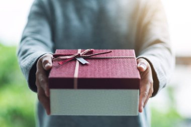 Kırmızı hediye kutusunu tutan ve veren bir kadının yakın plan görüntüsü.