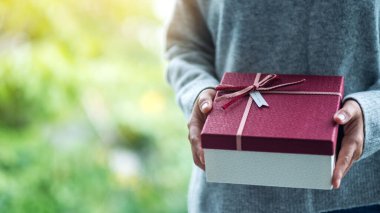 Kırmızı hediye kutusunu elinde tutan bir kadının yakın plan görüntüsü.