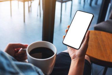 Kahve içerken elinde boş beyaz masaüstü ekranıyla cep telefonu tutan bir kadının görüntüsü