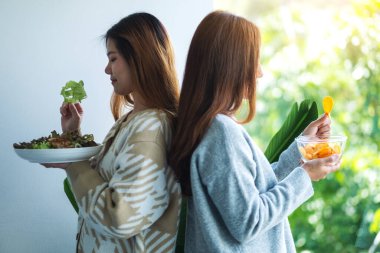 Sağlık hizmetleri konsepti için sebze salatası ve patates cipsi yemeyi seçen iki kadın.