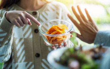 Sebze salatası yemeyi ve patates cipsini reddetmek için el işareti yapmayı seçen kadınlar.