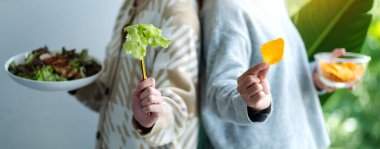 İki kadın, sağlık hizmetleri konsepti için sebze salatası ve patates cipsi tutuyor.