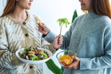 Sağlık sigortası konsepti için birbirine sebze salatası ve patates cipsi veren iki kadın.