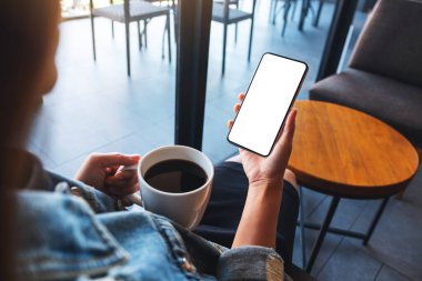 Kahve içerken elinde boş beyaz masaüstü ekranıyla cep telefonu tutan bir kadının görüntüsü