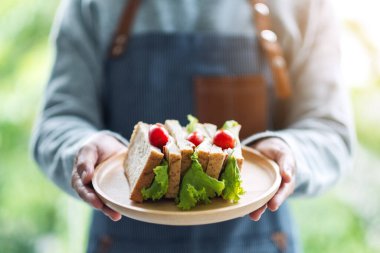 Yakından bakınca, elinde buğdaylı sandviçi ahşap tabakta servis eden bir garsonun resmi.