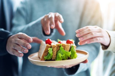 Bir grup insan yemek için tahtadan bir tabakta tam buğday sandviçi yiyor.