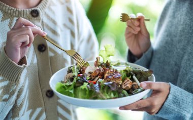 İki kadın tavuk salatasını birlikte tutuyor ve yiyorlar.
