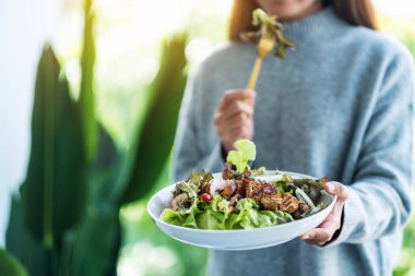 Elinde tavuk salatası tutan ve yiyen bir kadının yakın plan görüntüsü.