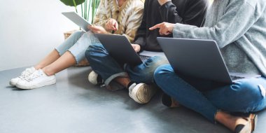 Bir grup genç birlikte oturup dizüstü bilgisayar ve dijital tablet kullanıyorlar.