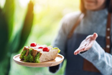 Yakından bakınca, servis yapan bir garsonun ahşap tabakta tüm buğday sandviçini gösterdiğini görüyoruz.