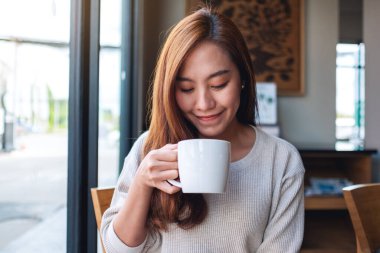 Kafede elinde kahve tutan ve içen Asyalı güzel bir kadının yakın plan görüntüsü.
