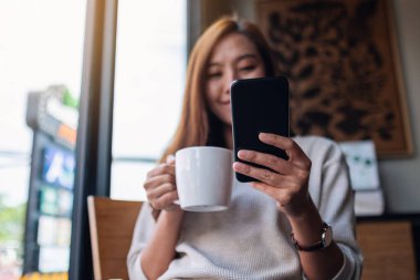 Kafede kahve içerken elinde cep telefonu tutan ve kullanan Asyalı güzel bir kadının yakın plan fotoğrafı.