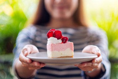 Yakından bakınca, Asyalı güzel bir kadının bir dilim çilekli keki tabakta tutarken ve verirken görüntüsü.