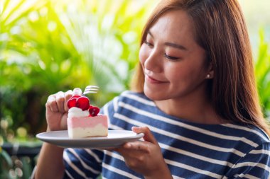Yakından bakınca, elinde çilekli kek tutan ve yiyen Asyalı güzel bir genç kadın görülüyor.