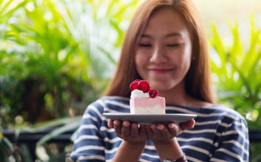 Yakından bakınca, Asyalı güzel bir kadının elinde bir dilim çilekli kek tuttuğunu görüyoruz.