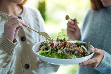 İki kadın tavuk salatasını birlikte tutuyor ve yiyorlar.