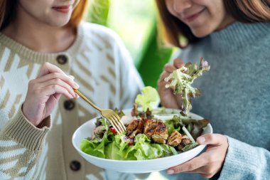 İki genç kadın tavuk salatasını birlikte tutuyor ve yiyor.
