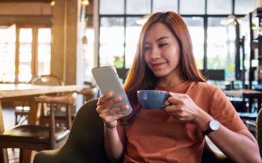 Kafede kahve içerken elinde cep telefonu tutan ve kullanan Asyalı güzel bir kadının yakın plan fotoğrafı.