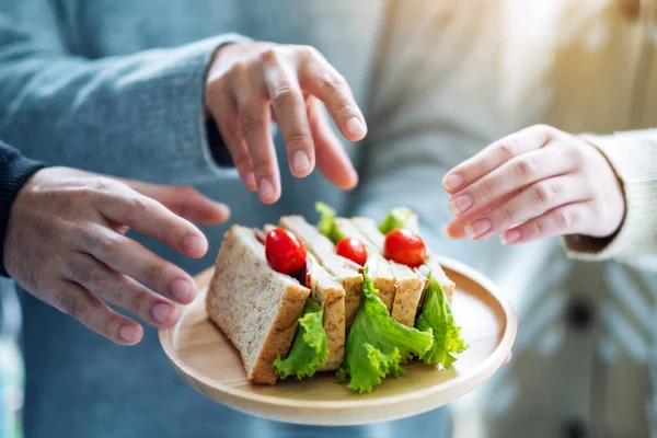 Bir grup insan yemek için tahtadan bir tabakta tam buğday sandviçi yiyor.
