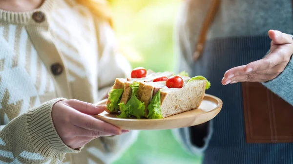 Bir garsonun ahşap tabakta tüm sandviçi müşteriye servis edişinin yakın plan fotoğrafı. 
