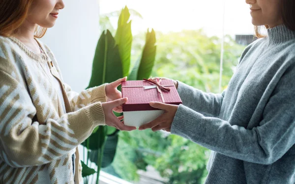 Arkadaşına hediye kutusu veren genç bir kadının yakın plan fotoğrafı. 