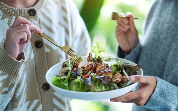 İki kadın tavuk salatasını birlikte tutuyor ve yiyorlar.