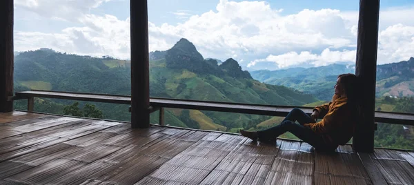 Dişi bir gezgin oturmuş, güzel dağlara bakıyor ve ahşap balkonda doğa manzarasına bakıyor.