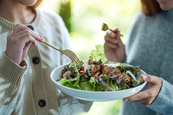 İki kadın tavuk salatasını birlikte tutuyor ve yiyorlar.