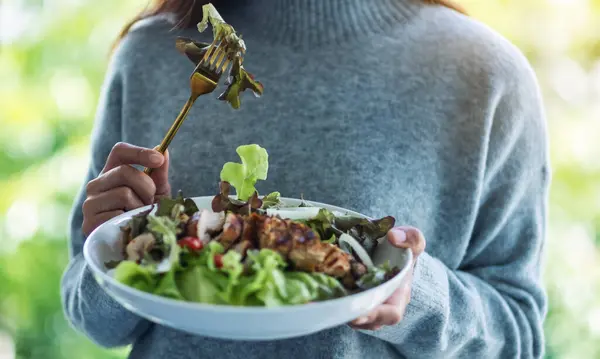 Elinde tavuk salatası tutan ve yiyen bir kadının yakın plan görüntüsü. 