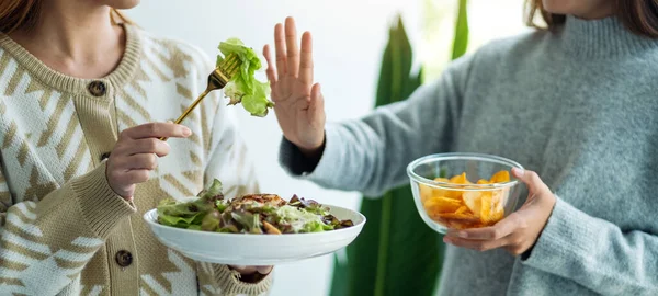 Kadınlar patates cipsi yemeyi ve sebze salatasını reddetmek için el işareti yapmayı seçiyorlar.