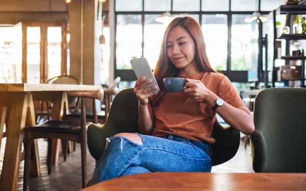 Kafede kahve içerken elinde cep telefonu tutan ve kullanan Asyalı güzel bir kadının yakın plan fotoğrafı.