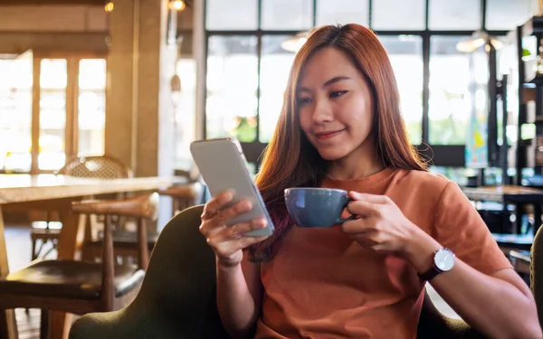 Kafede kahve içerken elinde cep telefonu tutan ve kullanan Asyalı güzel bir kadının yakın plan fotoğrafı.